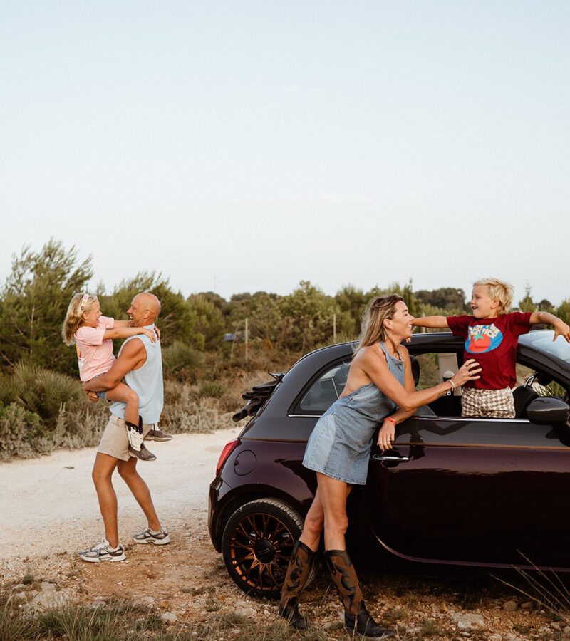 Natural outdoor family portrait of parents and two children in the car at the Montgo Mountain park in Javea, Alicante Spain